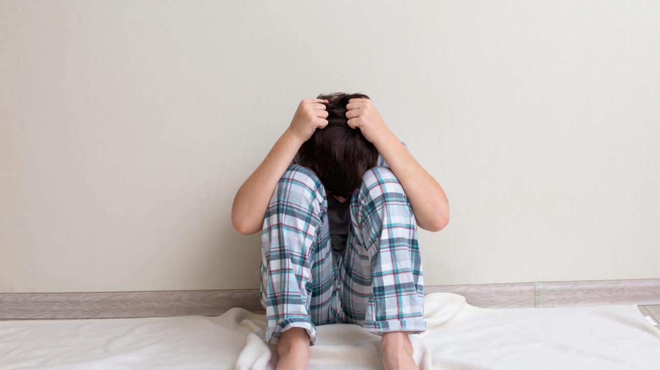 Anxious teen boy in pajamas sitting on the floor with hands on his head