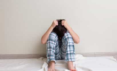 Anxious teen boy in pajamas sitting on the floor with hands on his head